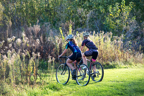 two people on bikes in grassy path with field and trees in background