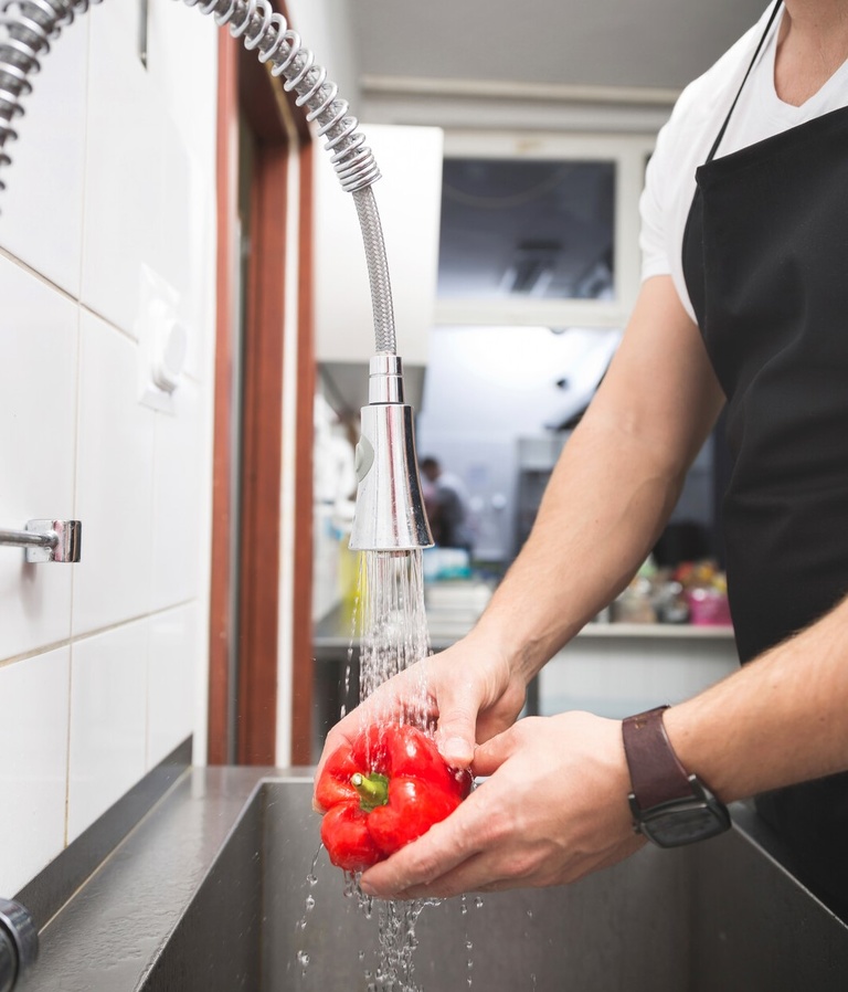 close up of worker washing a red pepper in a restaurant sink