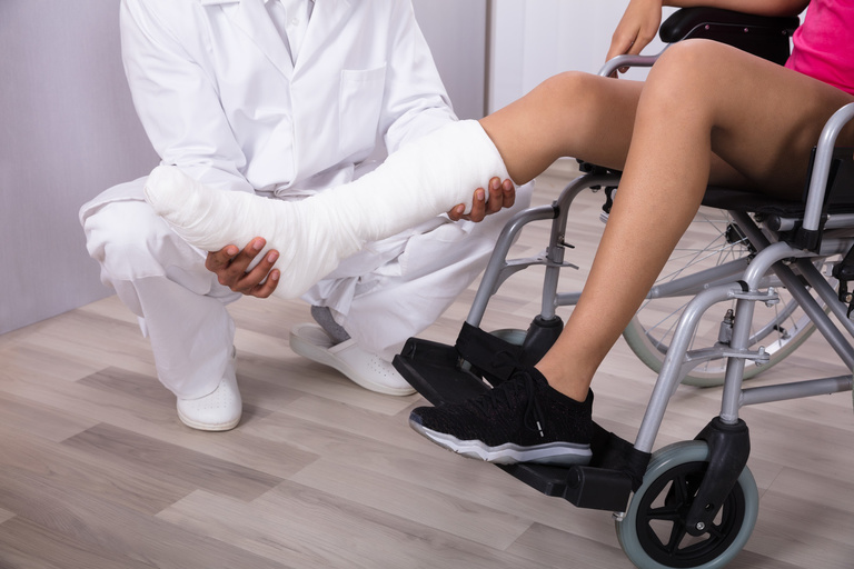 Medical provider holding the cast on leg of girl in wheelchair.
