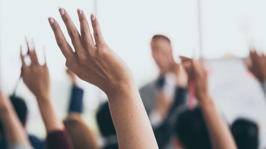 Group of raised hands in a meeting room.