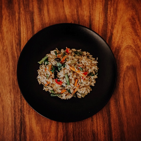 Black plate with vegetable fried rice set on wood table