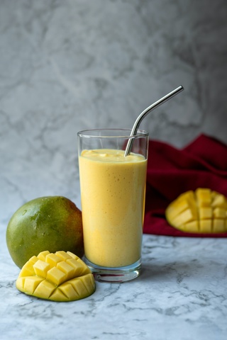 Smoothie in glass next to tropical fruits like papayas and mangoes