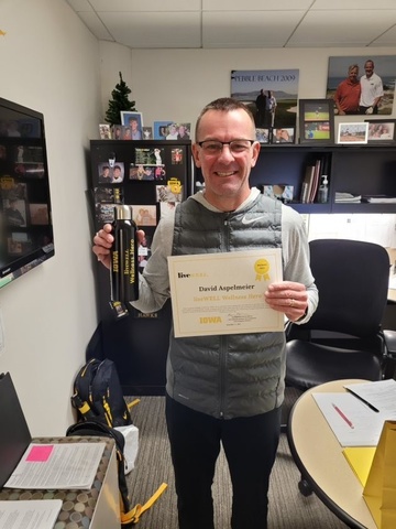 David Aspelmeir in office holding Wellness Hero certificate and liveWELL water bottle