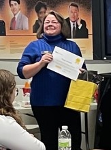 Dark haired woman smiles as she holds a certificate