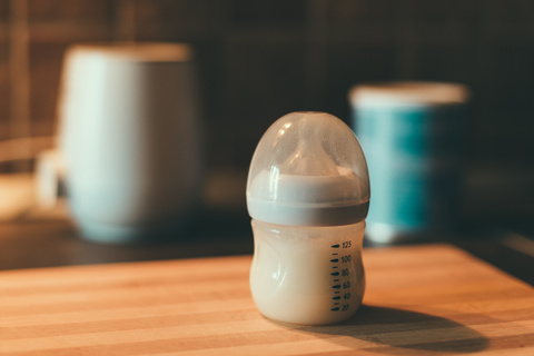 small baby bottle with breast pump blurred in background