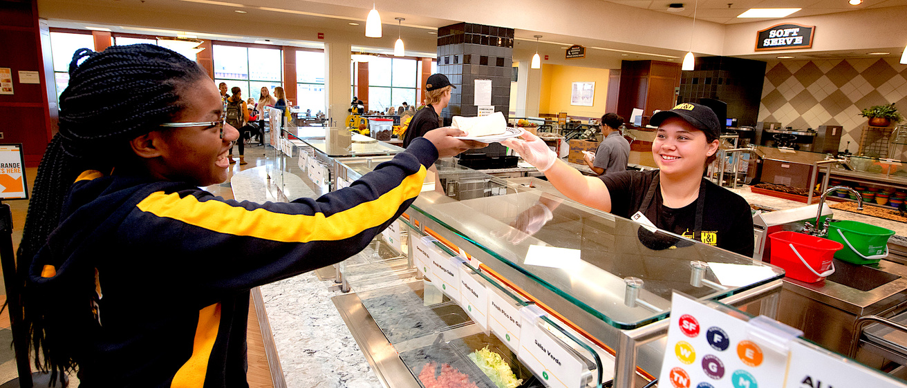 Student food service working passing an item over a counter to another person.