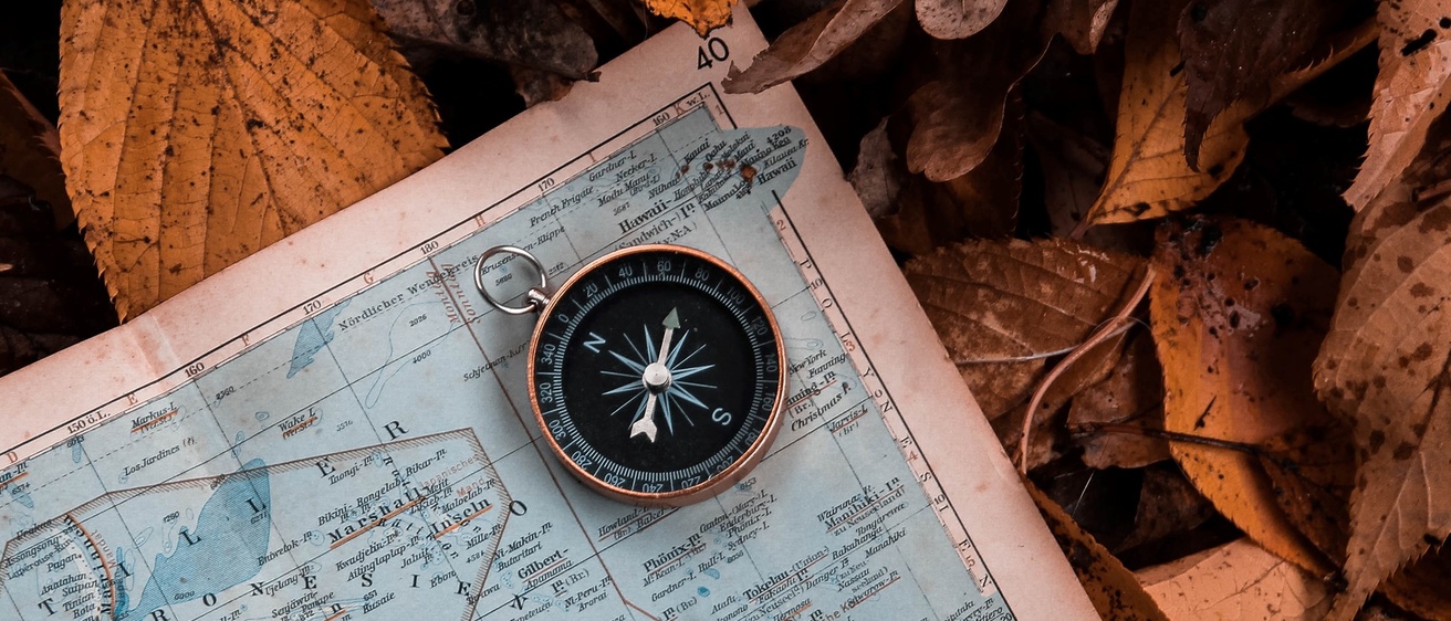 close-up of compass on a blue map and brown, dried leaves