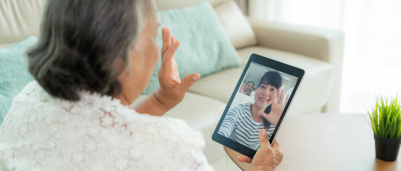 Back of older woman waving to person she is talking to via video call on hand-held device