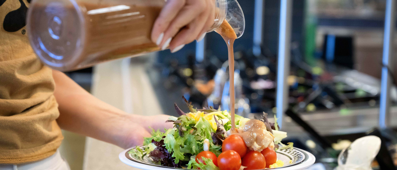A person pours salad dressing on their salad at Hillcrest Marketplace