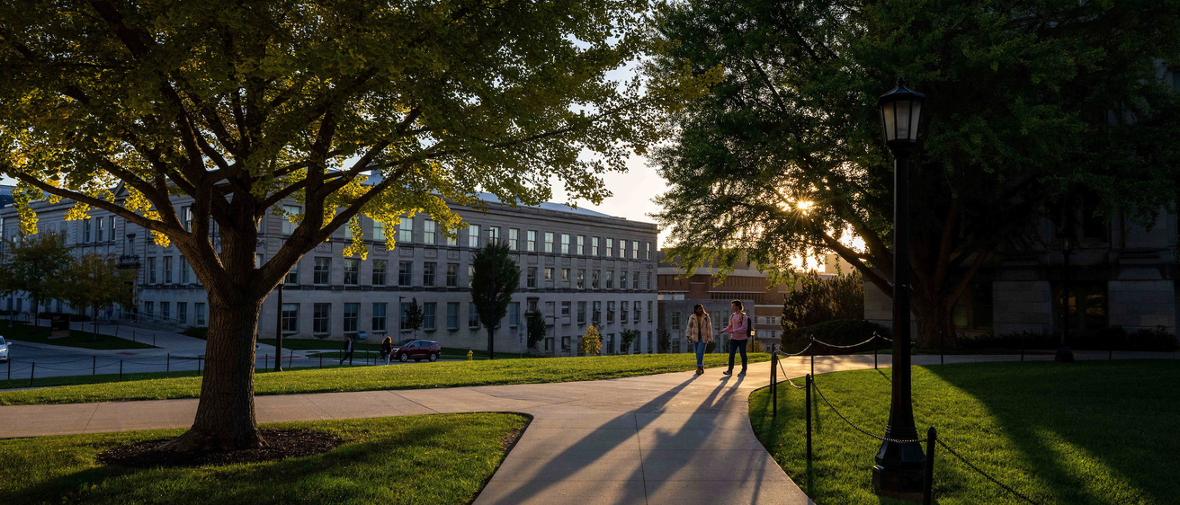 two individuals walking through trees on campus