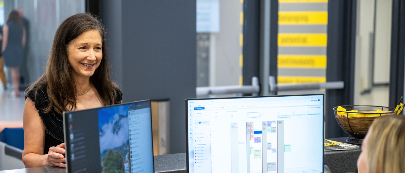 Two University of Iowa employees talk at a desk during the workday