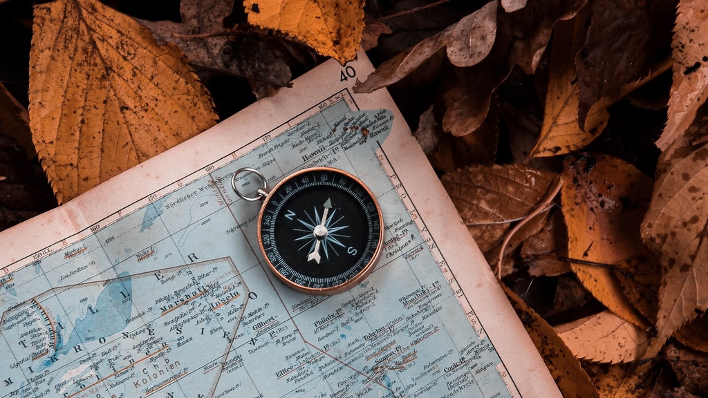 close-up of compass on a blue map and brown, dried leaves