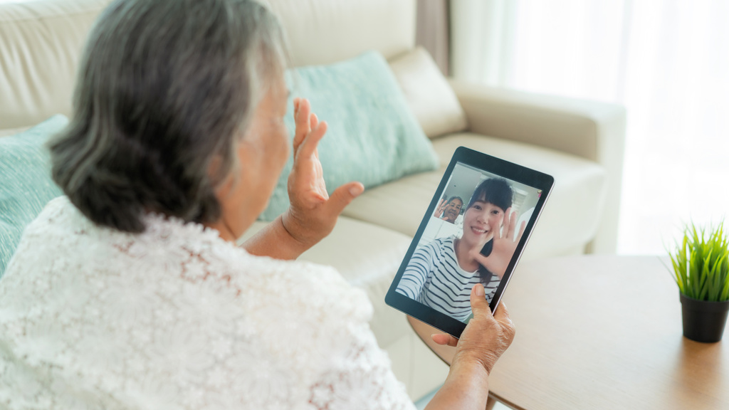 Back of older woman waving to person she is talking to via video call on hand-held device
