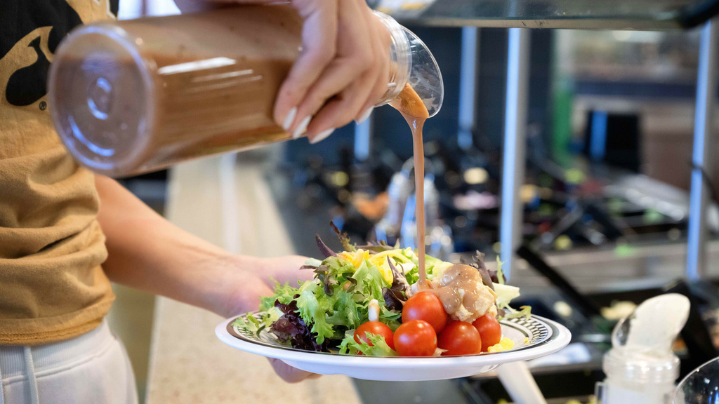 A person pours salad dressing on their salad at Hillcrest Marketplace