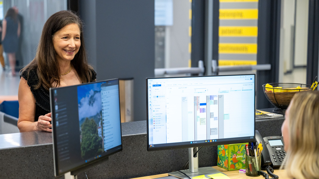 Two University of Iowa employees talk at a desk during the workday