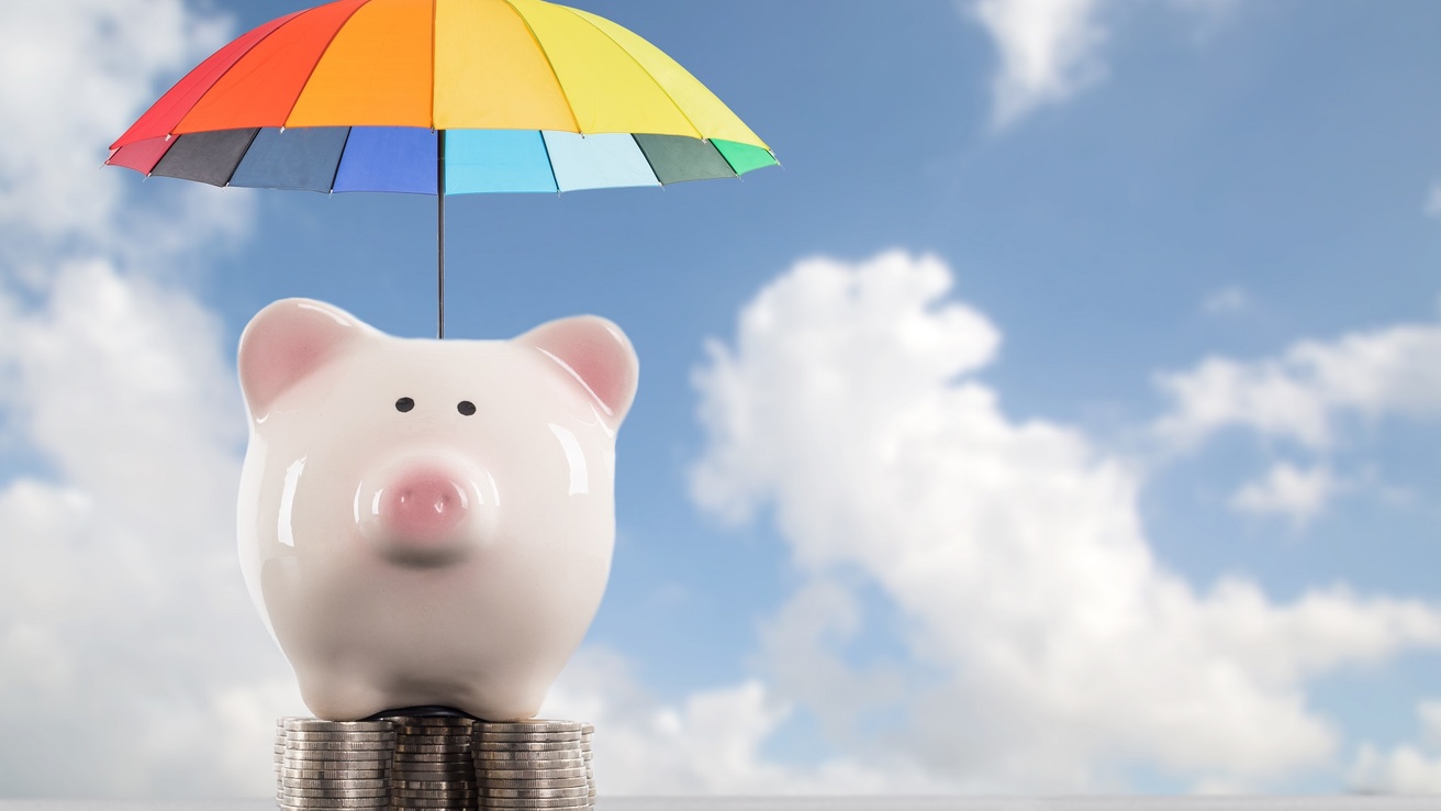 Umbrella above a white piggy bank standing on a stack of silver coins
