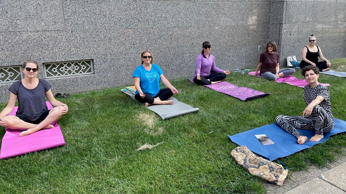women sitting cross-legged on yoga mats on grass next to the UI libray