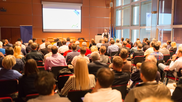 Audience viewing a presentation on a screen with the presenter at the front of the room