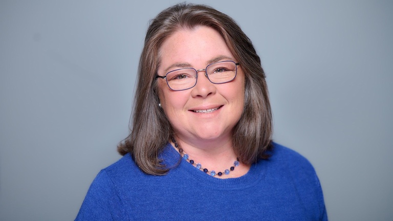 Headshot of smiling brunette woman with glasses in blue sweater